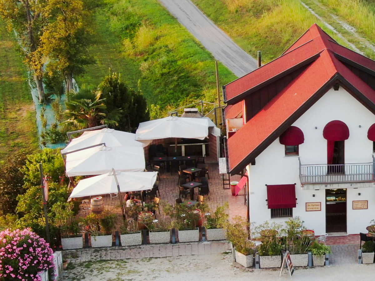 Il dehors dell'osteria: tavolini e ombrelloni bianchi davanti alla casa col tetto rosso
