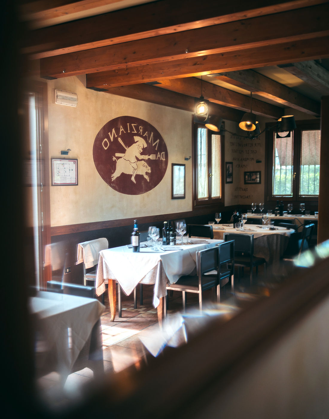 La sala dell'osteria con le travi di legno e i tavoli apparecchiati di bianco