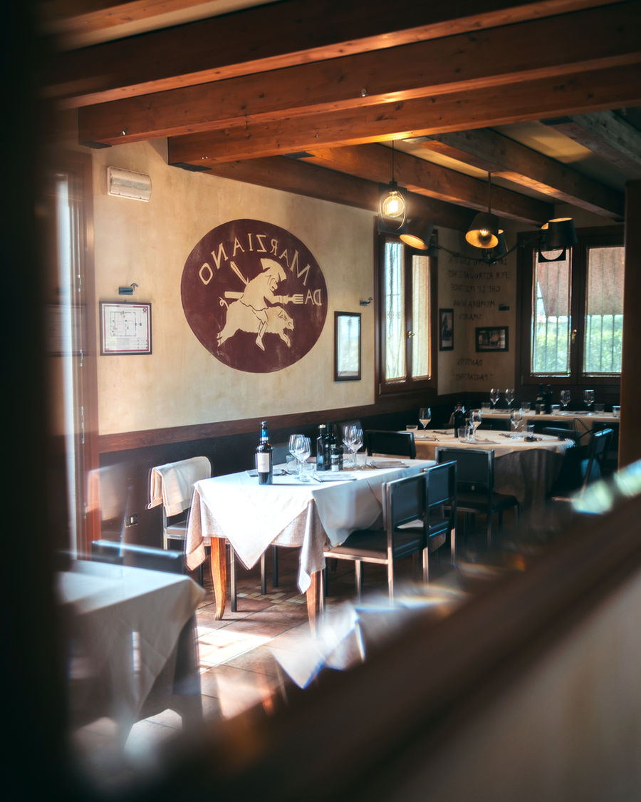 La sala dell'osteria vista dalla porta: travi di legno, tovaglie bianche e un vecchio stemma dipinto sul muro