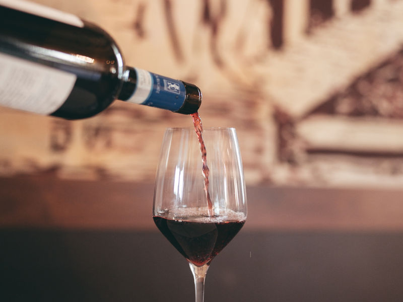 Una bottiglia di vino rosso adagiata davanti alla parete di etichette dell'osteria